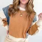 Woman wearing a brown and beige sweater with denim sleeves against a white background