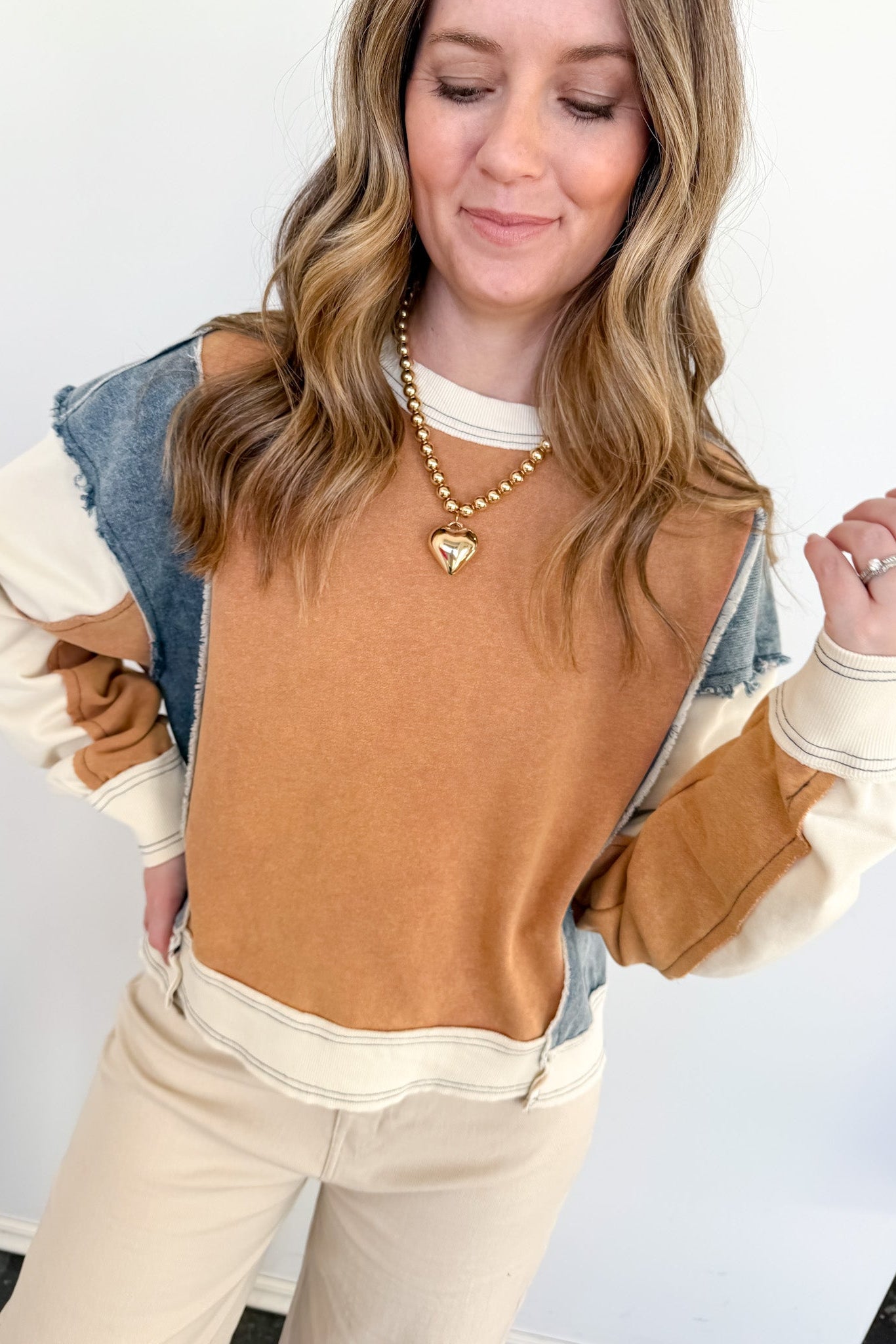 Woman wearing a brown and beige sweater with denim sleeves against a white background