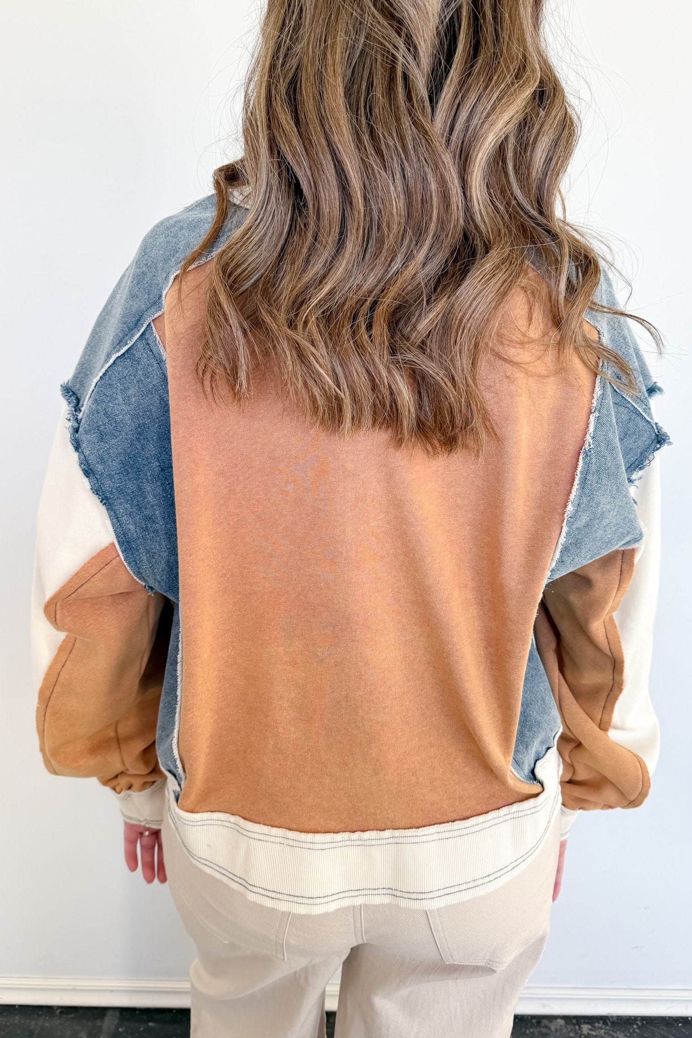 Person wearing a mustard yellow top and denim jacket with beige pants against a white background