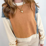 Woman wearing a brown top with denim sleeves and beige pants against a white wall.