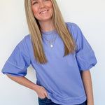 Woman wearing a blue oversized t-shirt and jeans against a white wall