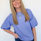 Woman wearing a blue oversized t-shirt and jeans against a white wall