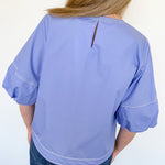 Person wearing a light blue blouse with a plain background