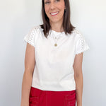 Woman wearing a white top with lace sleeves and red pants against a plain background