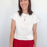 Woman wearing a white top with lace sleeves and red pants against a plain background