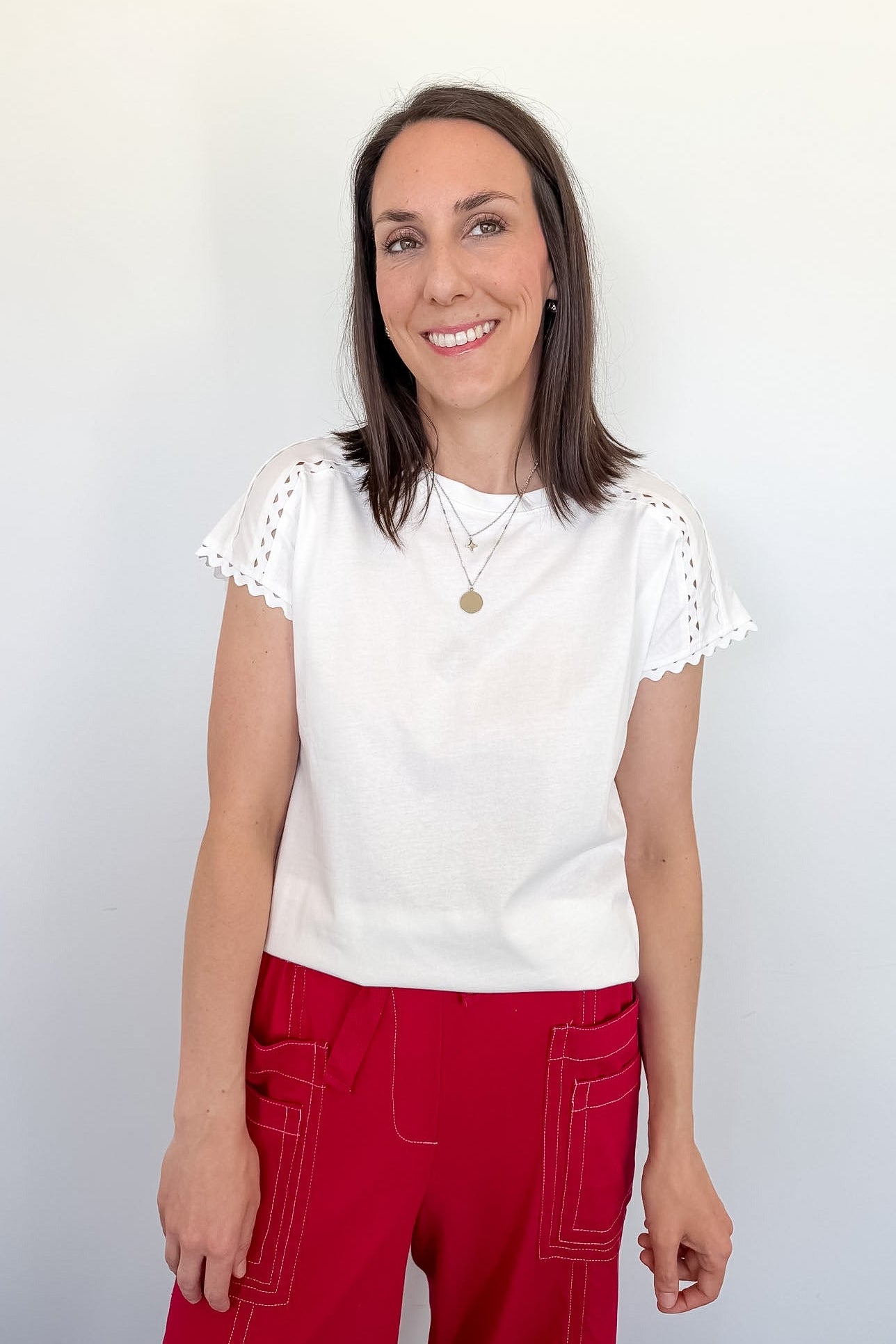 Woman wearing a white top with lace sleeves and red pants against a plain background