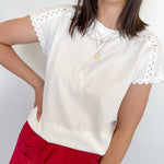 Woman wearing a white top in front of a white wall with red pants.