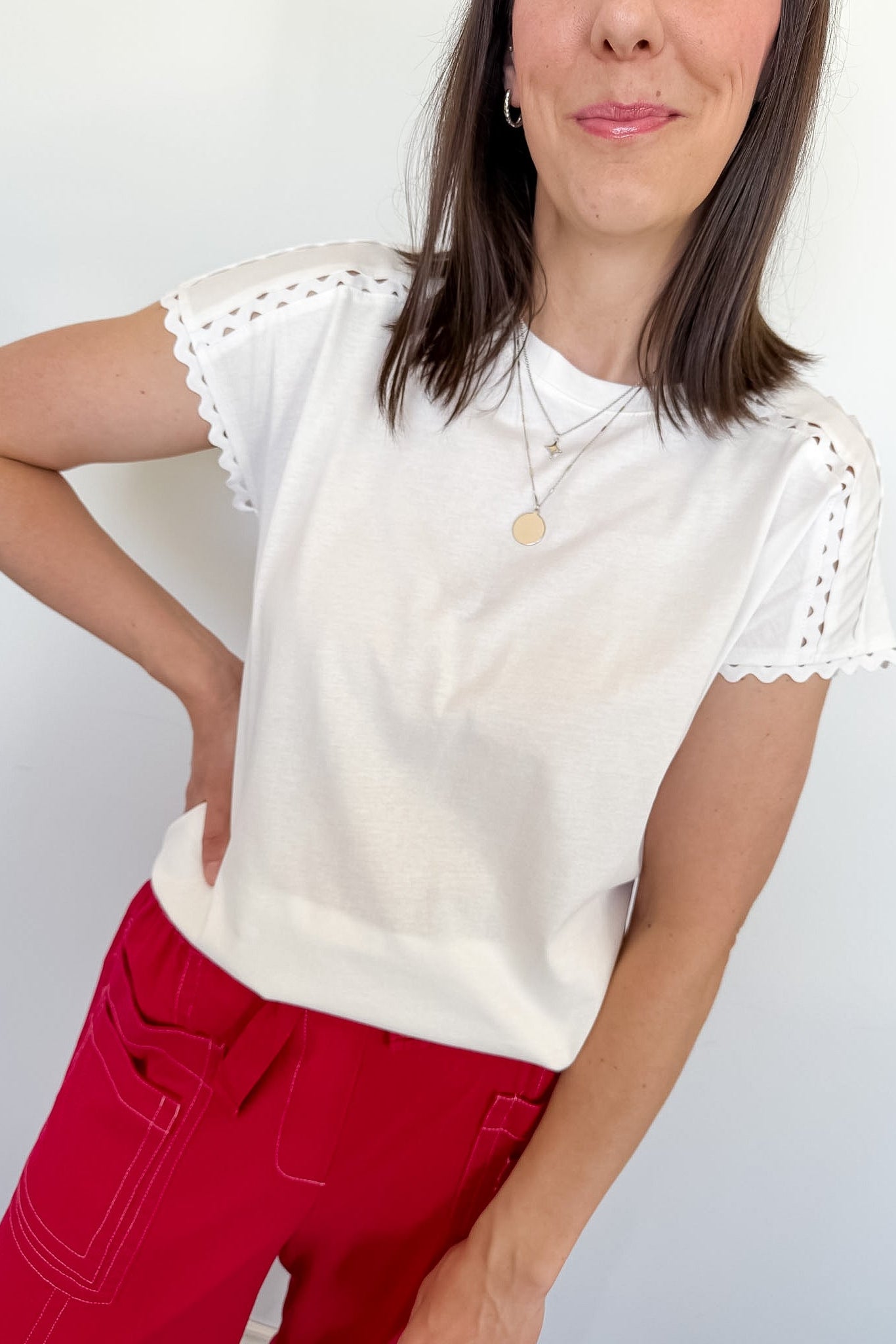 Woman wearing a white top in front of a white wall with red pants.