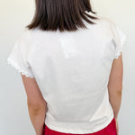 Woman standing in front of a white wall with her back to the camera with a white blouse on.