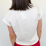 Woman standing in front of a white wall with her back to the camera with a white blouse on.