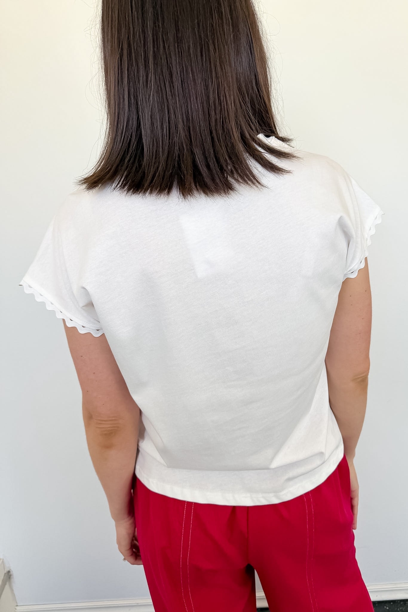Woman standing in front of a white wall with her back to the camera with a white blouse on.