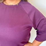 Person wearing a purple long-sleeve shirt with a plain background