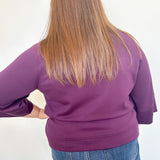 Person wearing a purple shirt and blue jeans with a plain white background