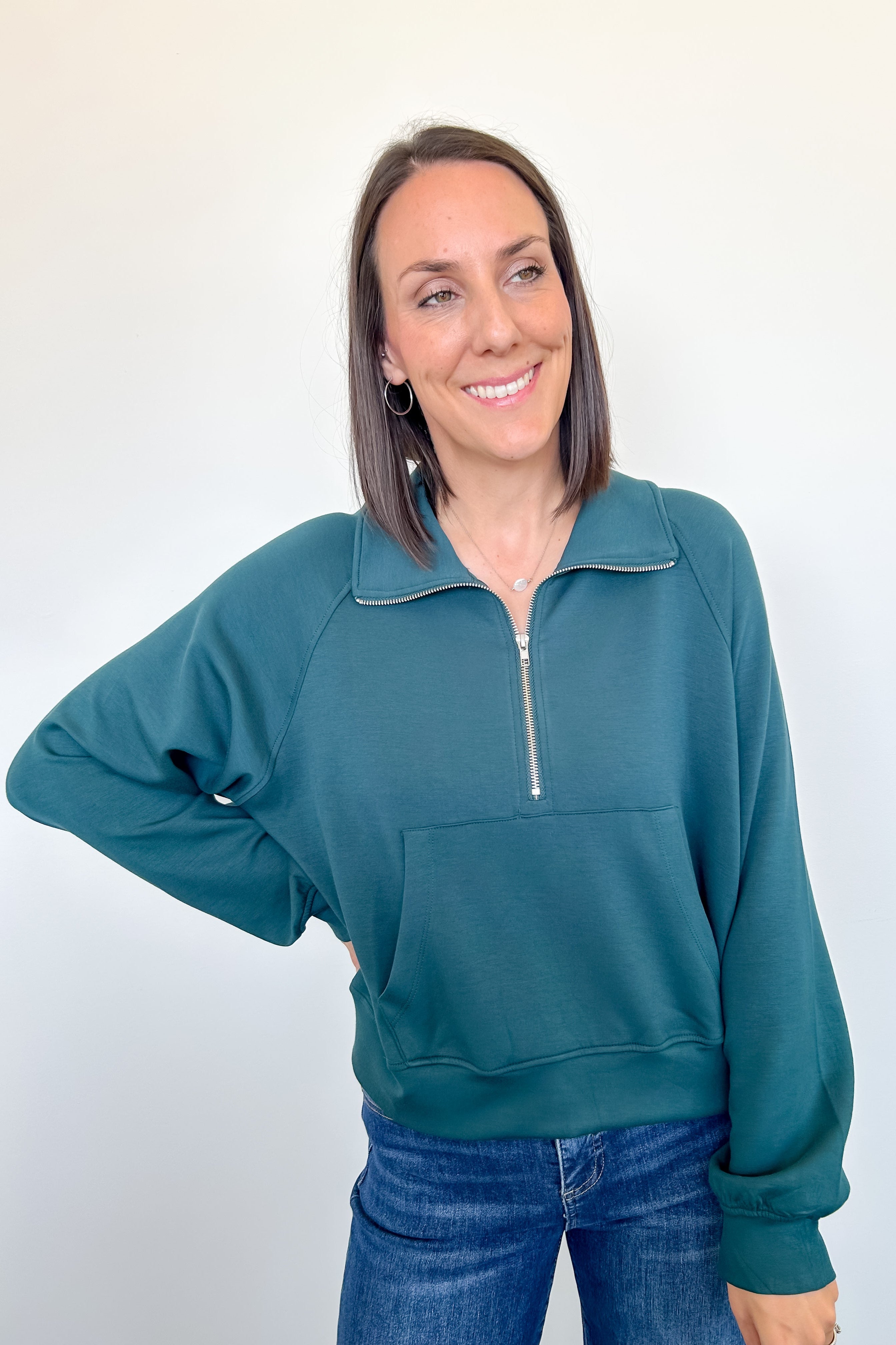 Woman wearing a teal pullover with a zipper on a white background