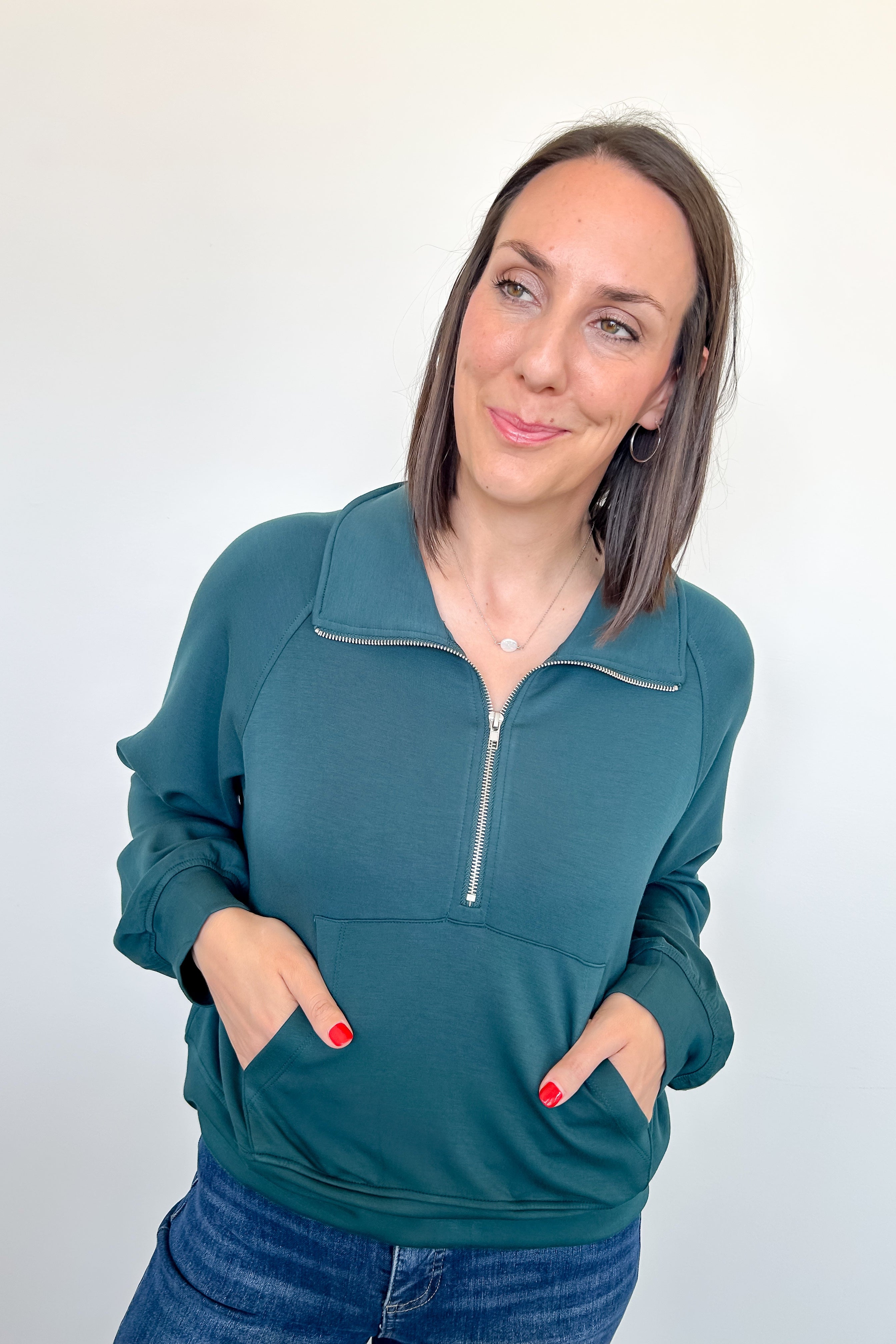 Woman wearing a teal zip-up sweatshirt against a white background