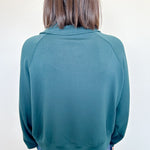 Person wearing a teal sweater and blue jeans against a white wall