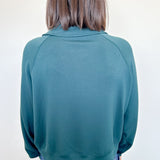 Person wearing a teal sweater and blue jeans against a white wall