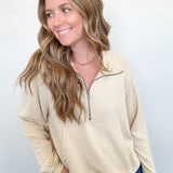 Woman wearing a beige long-sleeve shirt with a quarter zip on a white background