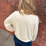 Woman in front of a brick wall wearing a beige sweatshirt and jeans.