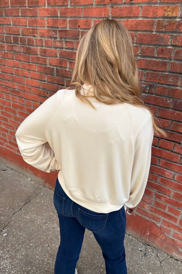 Woman in front of a brick wall wearing a beige sweatshirt and jeans.