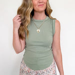 Woman wearing a green sleeveless top and floral pants against a white background