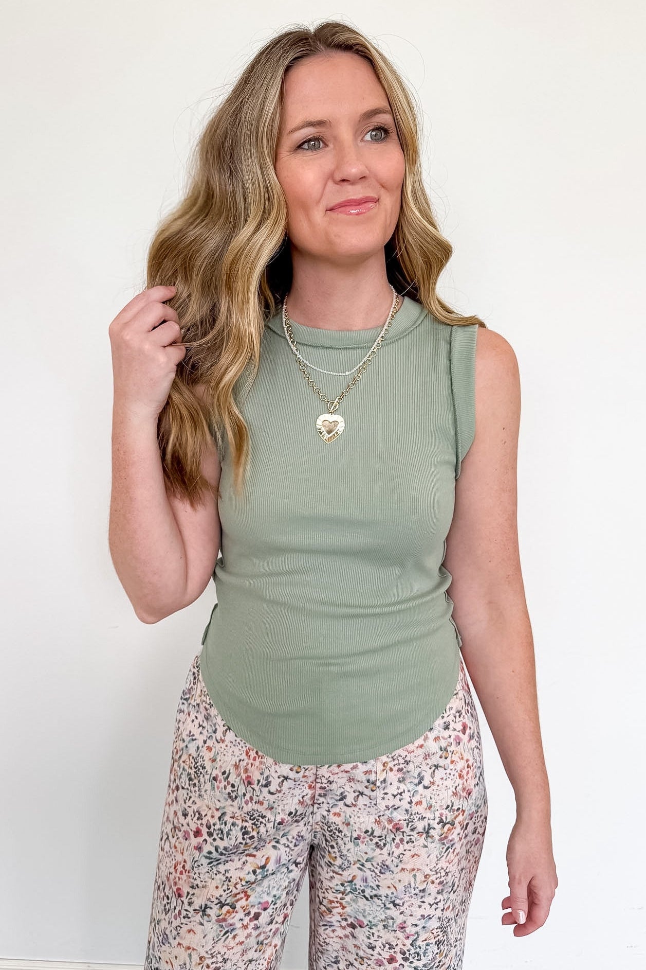Woman wearing a green sleeveless top and floral pants against a white background