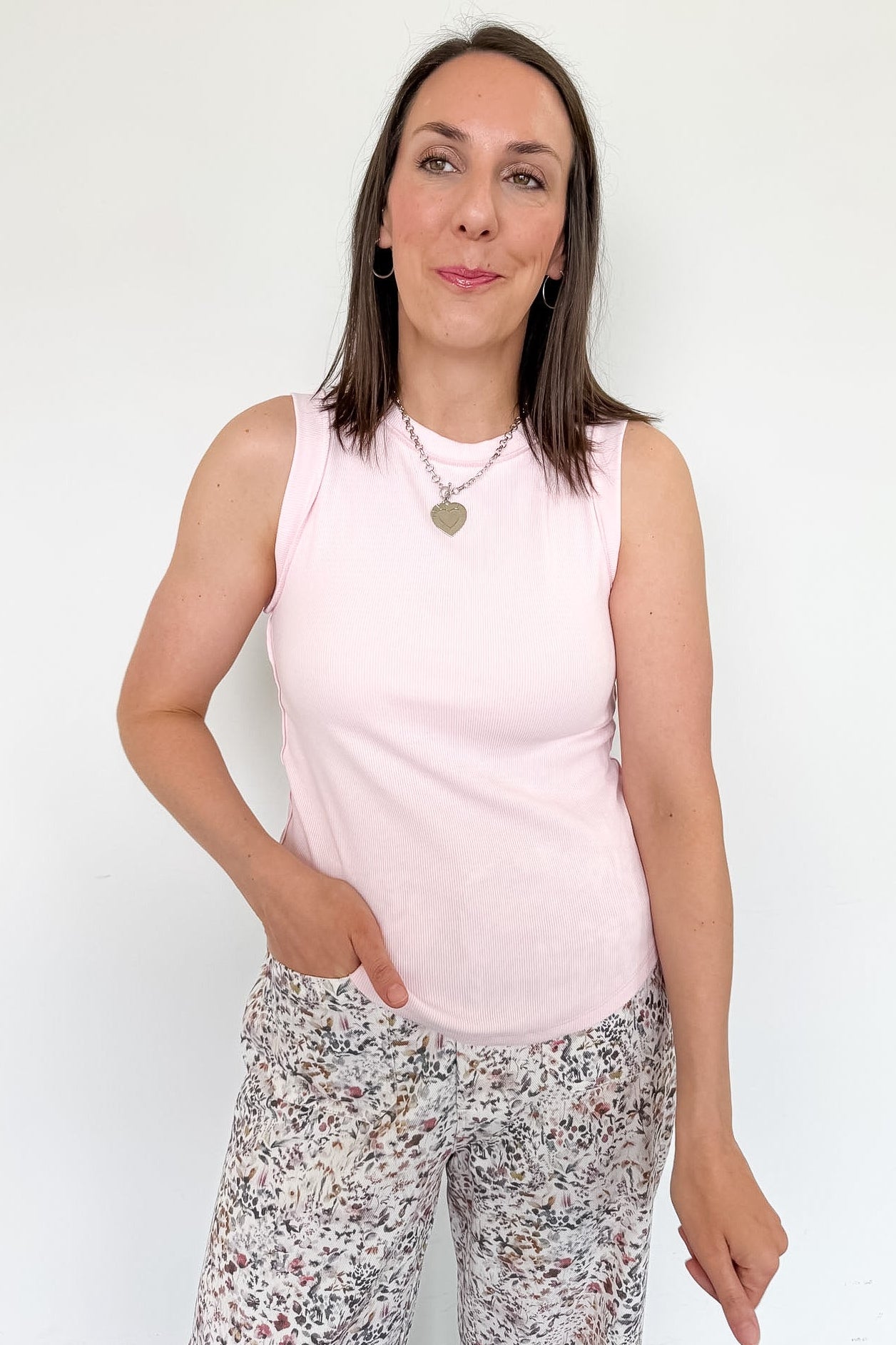 Woman wearing a light pink sleeveless top and patterned pants against a white background