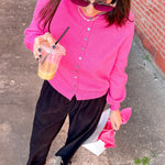 Woman in a pink cardigan and black pants holding a drink on a sidewalk.