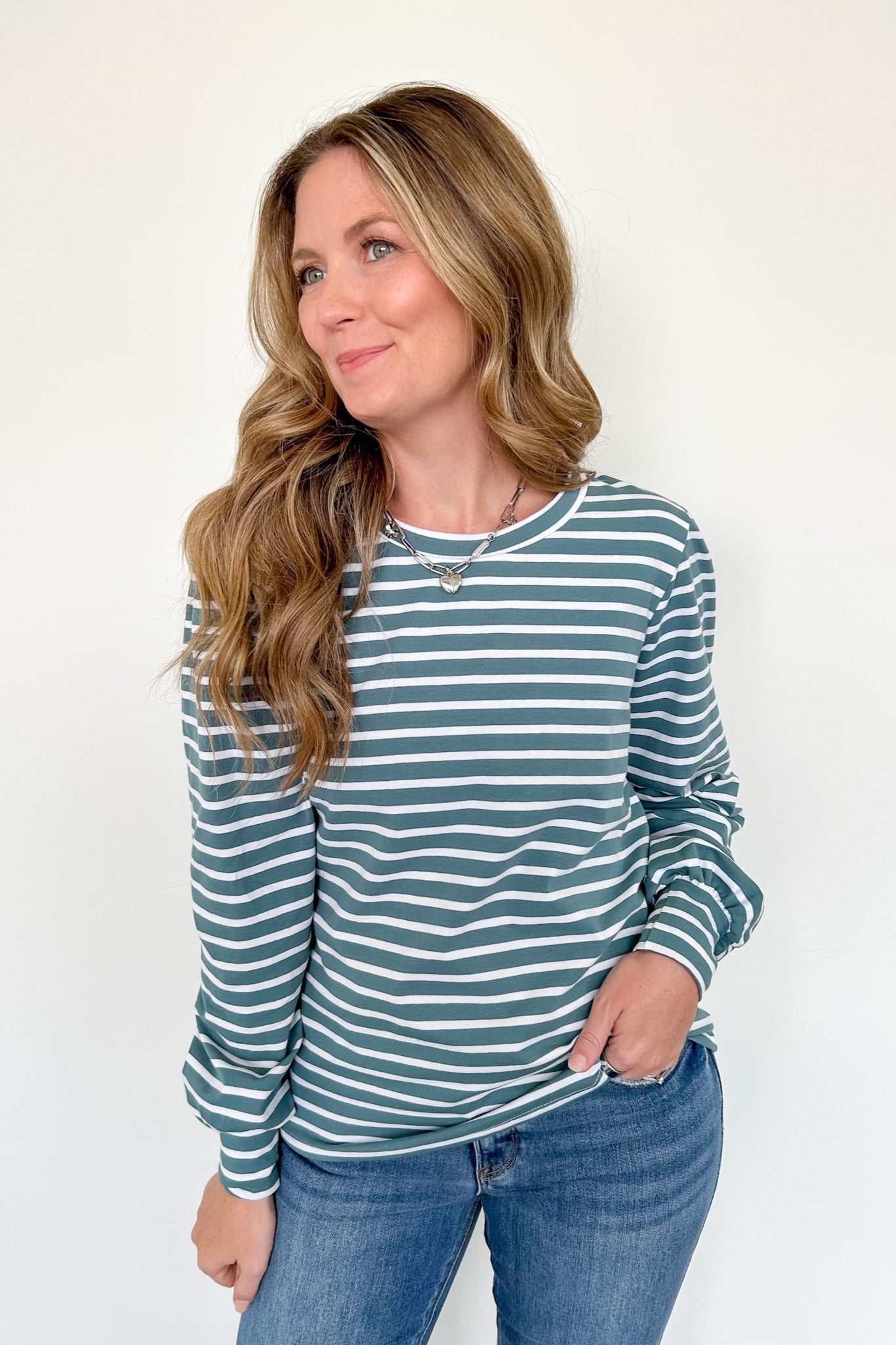 Woman wearing a striped long-sleeve shirt and jeans against a white background