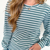 Woman wearing a green and white striped long-sleeve top with blue jeans on a white background