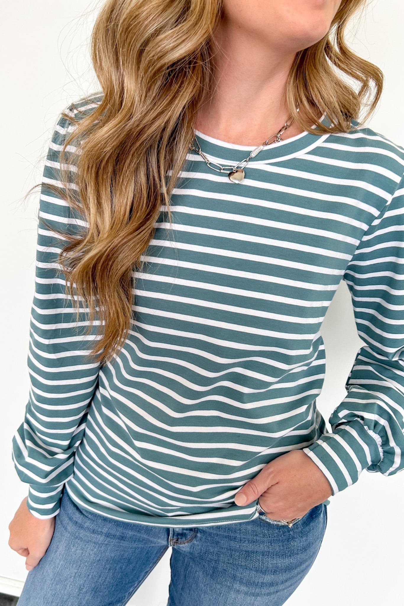 Woman wearing a green and white striped long-sleeve top with blue jeans on a white background