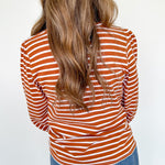Person wearing a rust and white striped long-sleeve top and blue jeans against a white background