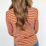 Person wearing a rust and white striped long-sleeve top and blue jeans against a white background