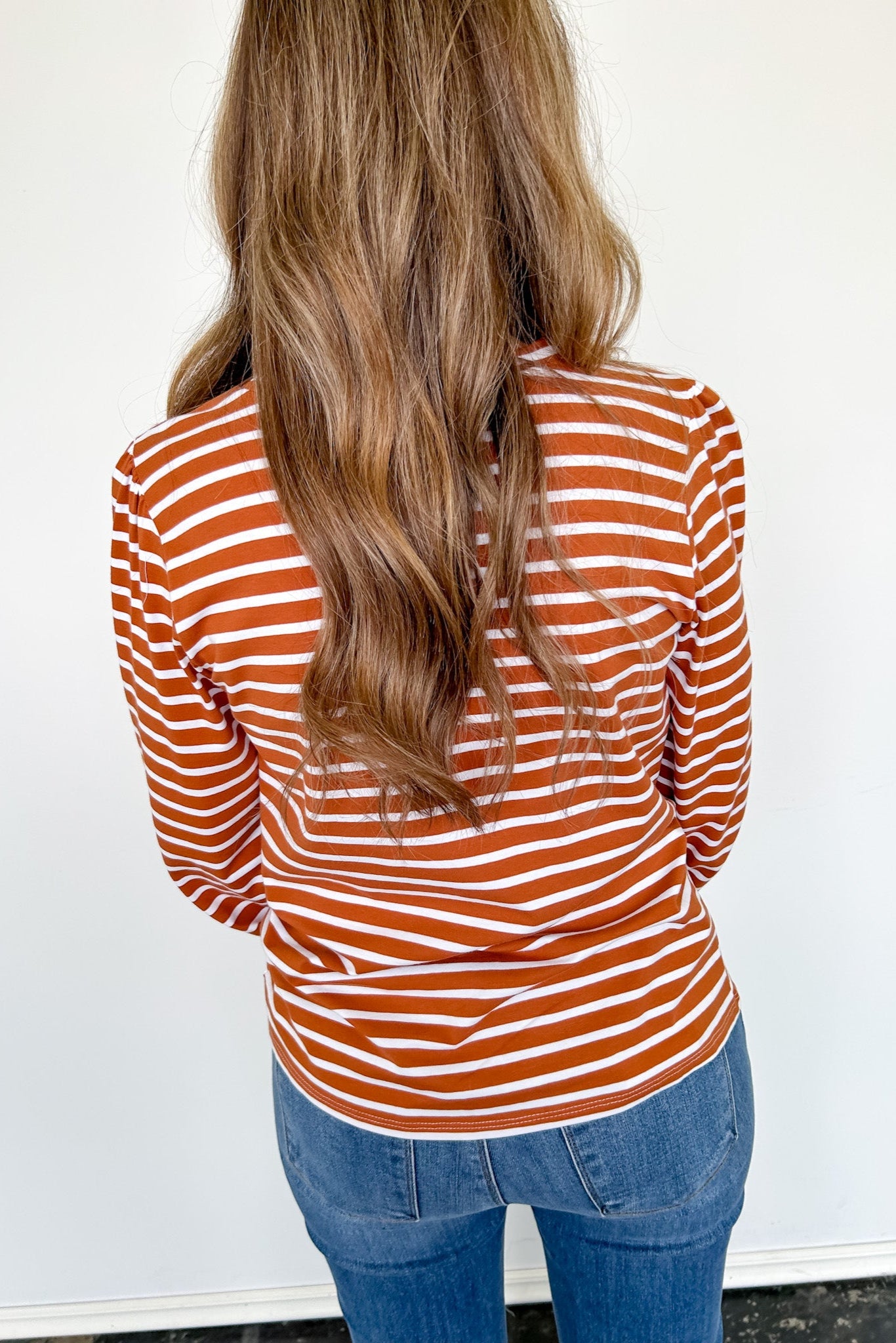 Person wearing a rust and white striped long-sleeve top and blue jeans against a white background