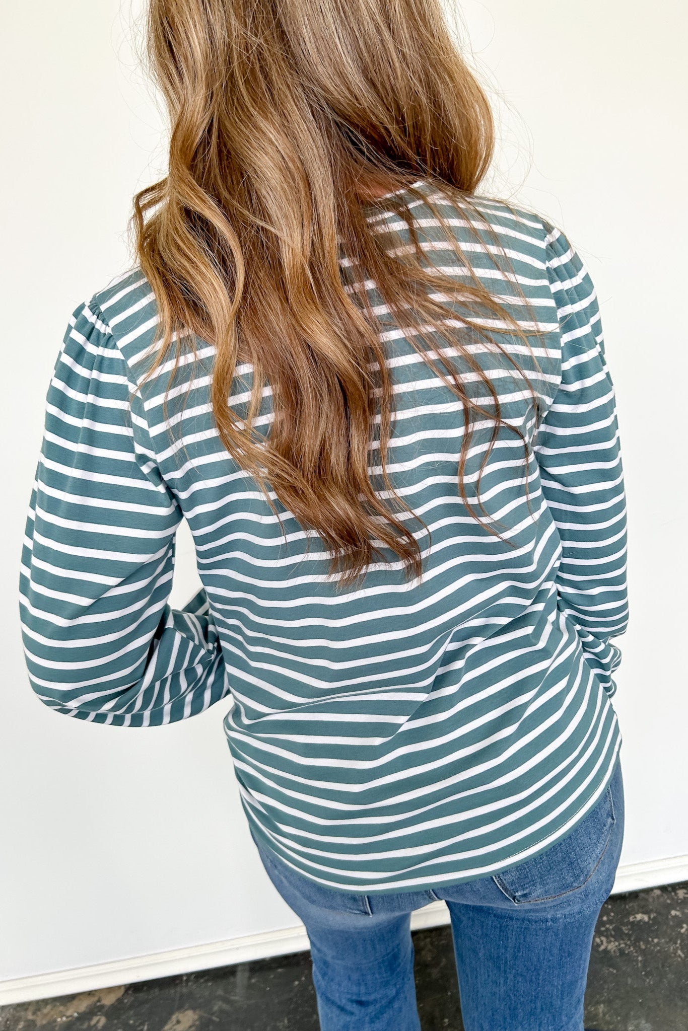 Person wearing a green and white striped long-sleeve shirt with blue jeans against a white background