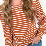 Person wearing a rust and white striped long-sleeve top with blue jeans on a white background