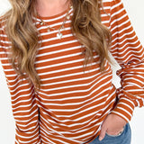 Person wearing a rust and white striped long-sleeve top with blue jeans on a white background