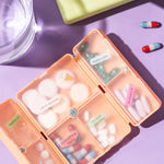 Colorful pill organizer with assorted pills and a glass of water on a purple background