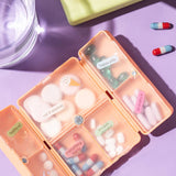 Colorful pill organizer with assorted pills and a glass of water on a purple background