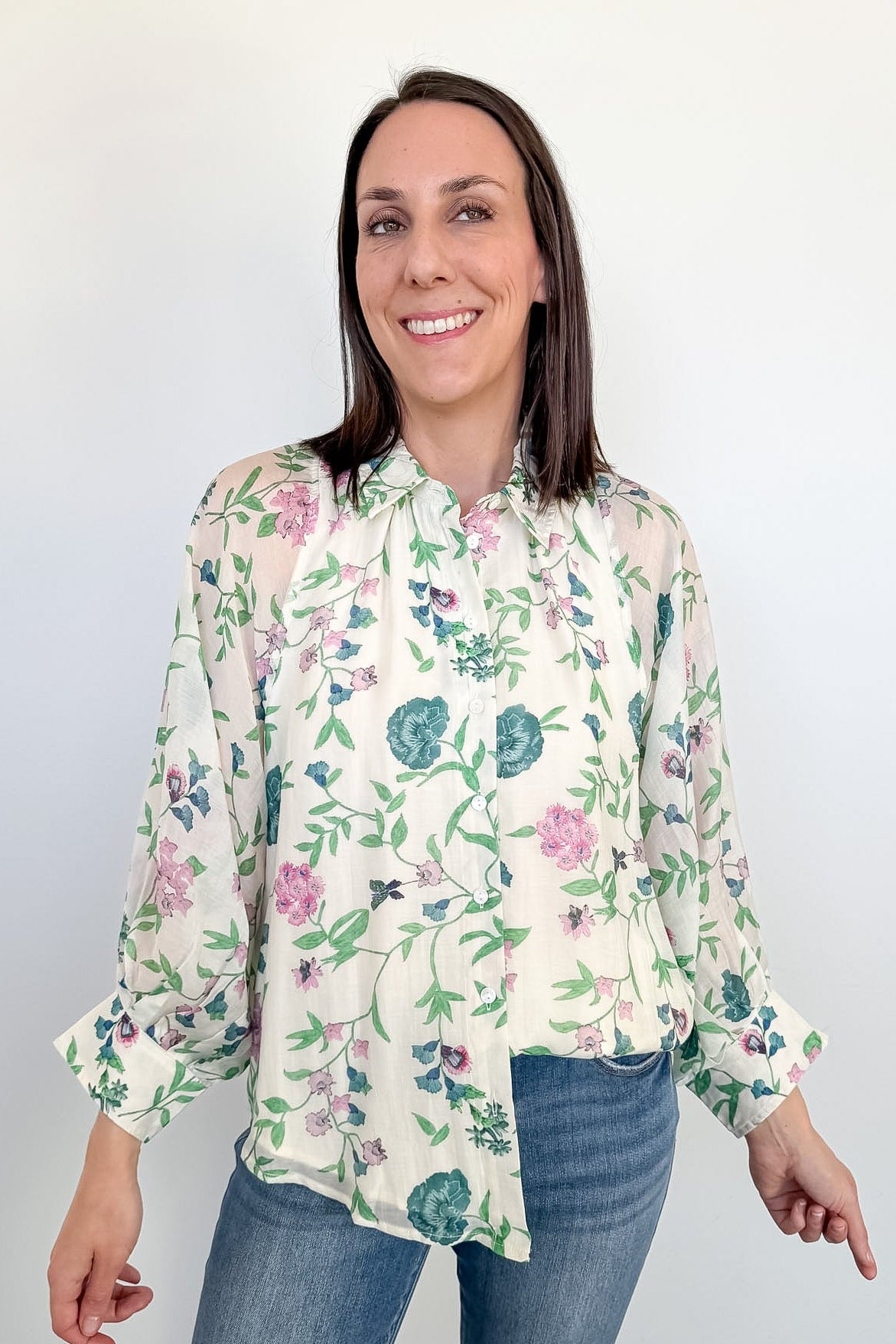 Woman wearing a floral blouse and jeans against a white background