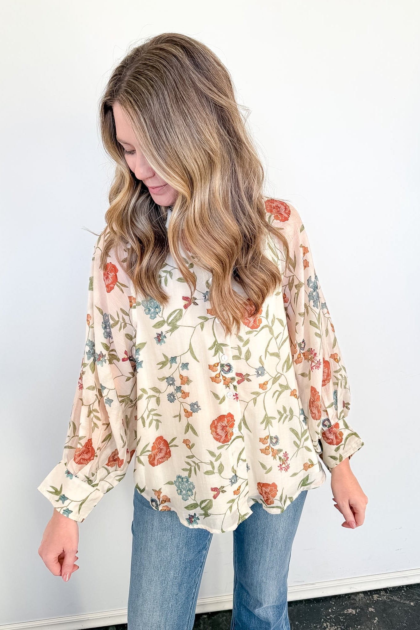 Woman wearing a floral blouse and jeans against a white background
