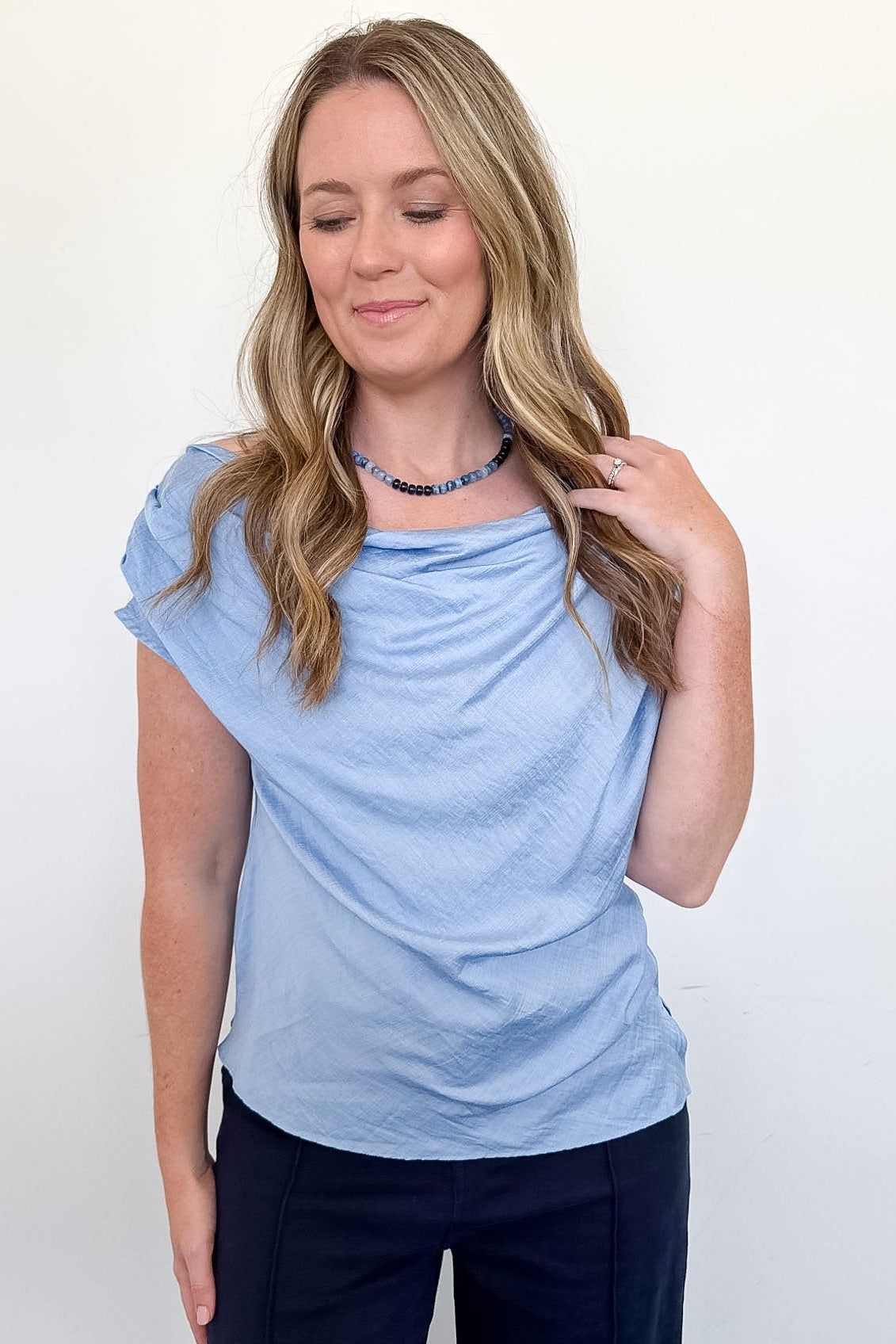 Woman wearing a light blue top and dark pants against a white background
