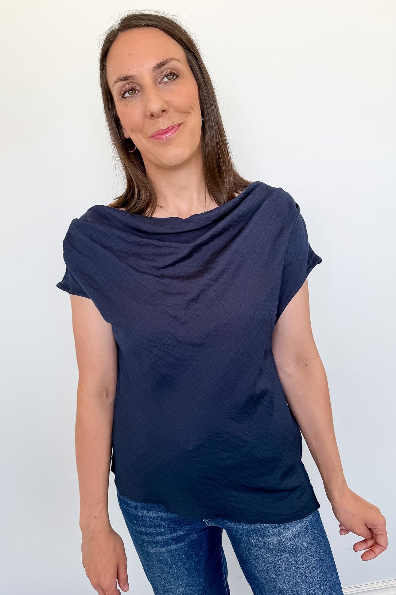 Woman wearing a navy blue cowl-neck top and jeans against a white background