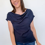 Woman wearing a navy blue top and blue jeans against a white wall