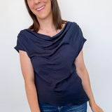 Woman wearing a navy blue top and blue jeans against a white wall