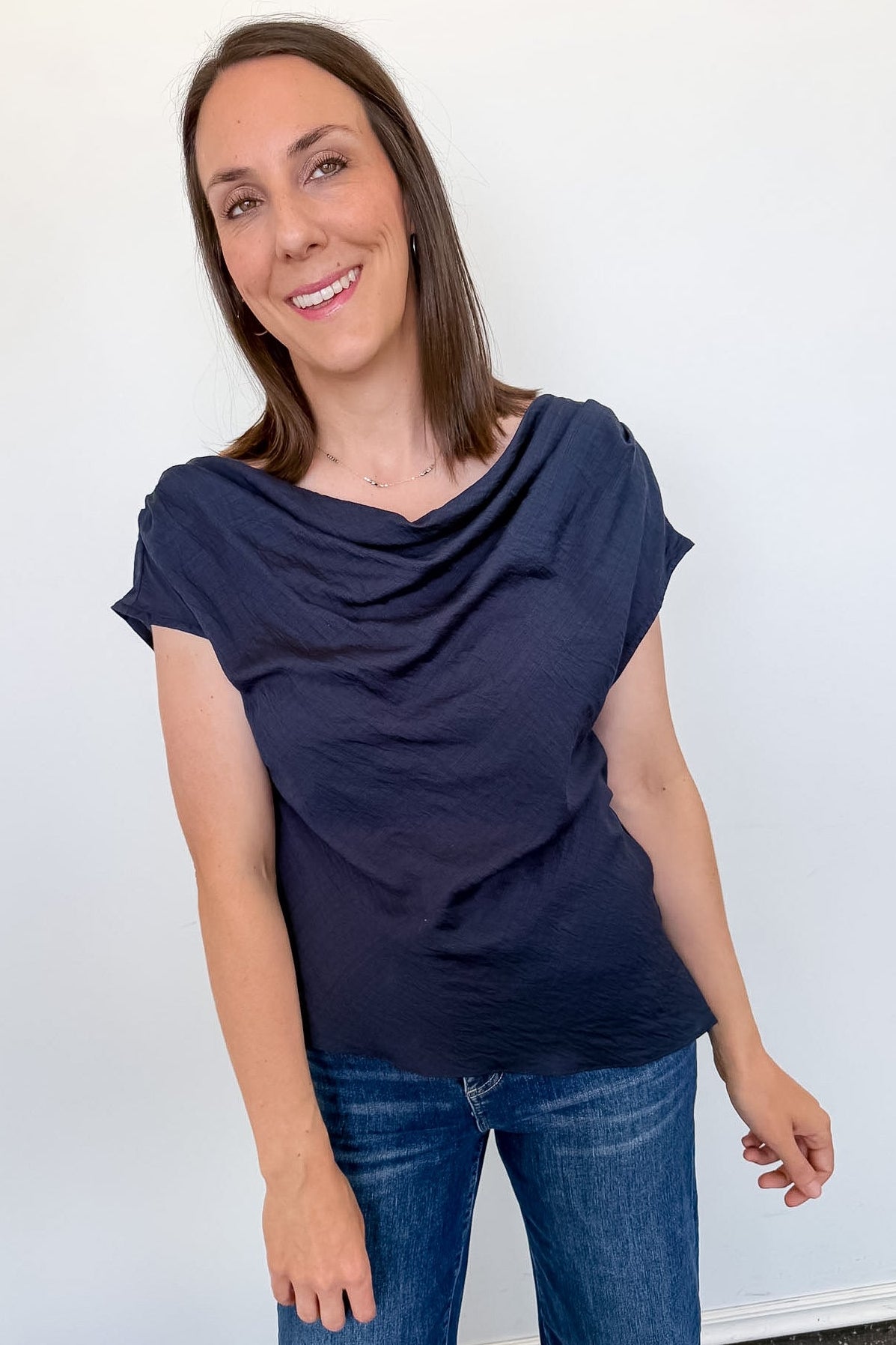 Woman wearing a navy blue top and blue jeans against a white wall