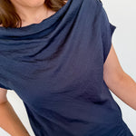 Woman wearing a navy blue top and blue jeans against a white wall.