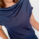 Woman wearing a navy blue top and blue jeans against a white wall.
