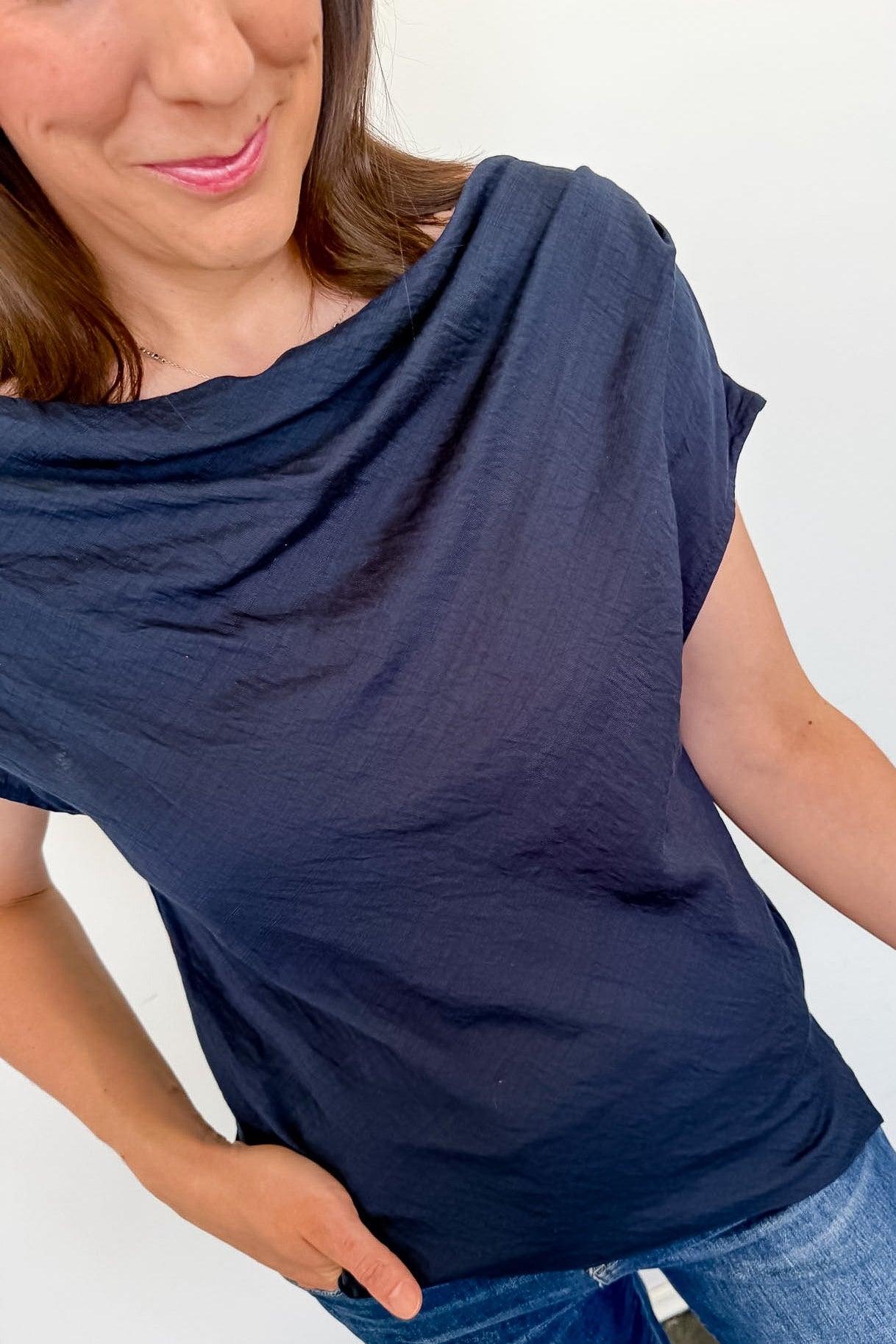 Woman wearing a navy blue top and blue jeans against a white wall.