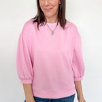 Woman wearing a pink sweatshirt and blue jeans against a white background